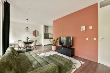 Konforlu yeşil kanepe, televizyon ünitesi ve minimalist yemek alanının bulunduğu çağdaş bir oturma odası. Bu alan zarafet ve konforu şık tasarımlarla birleştirir.