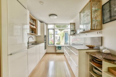 Beyaz dolaplı gösterişli ve çağdaş bir mutfak, büyük pencerelerden gelen doğal ışık, ve basitlik ve işlevsellik saçan bir estetik..