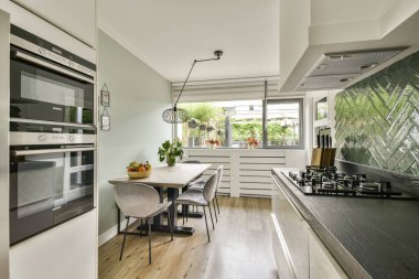 Geniş ve çağdaş bir mutfak. Parlak aletler, yemek alanı ve bol miktarda doğal ışık sağlayan geniş pencereler var..