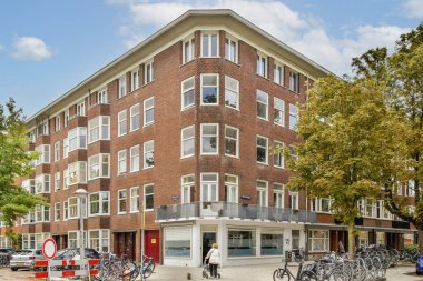 Modern şehir mimarisinin çarpıcı bir örneği geniş pencereler ve benzersiz bir üçgen cephe sergiliyor. Sahne, etrafındaki ağaçlar ve bisikletlerle güçlendiriliyor..