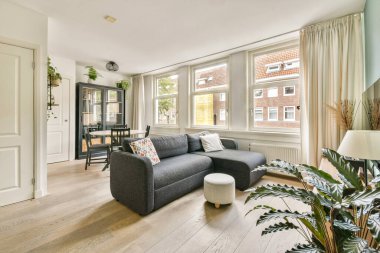 Rahat mobilyaların sergilendiği rahat modern oturma odası, geniş pencerelerden bol miktarda doğal ışık ve kapalı alandaki bitkilerin yeşillik dokunuşu..