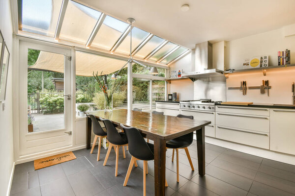 Просторная современная кухня с большими окнами, обеспечивающими естественное освещение, сонный шкаф и стильный обеденный стол для наслаждения приготовлением пищи.