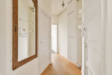 Geniş bir koridorda ayna, beyaz panelli kapılar ve ahşap döşemeler var. Evde parlak ve davetkar bir atmosfer yaratıyorlar..
