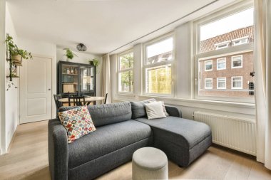 Rahat bir kesimlik kanepe, büyük pencerelerden gelen doğal ışık ve rahat atmosferi geliştiren çağdaş dekorun yer aldığı modern bir oturma odası..