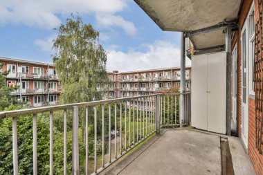 Modern bir apartman balkonundan sakin bir manzara bitişik binayı ve yemyeşil alanı gösteriyor. Açık havada sakin bir günün tadını çıkarmak için mükemmel..