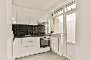 Gösterişli, modern bir mutfak. Minimalist beyaz dolaplar ve siyah seramik kaplama. Bol miktarda doğal ışık, şık bir ortam için alanı geliştirir..