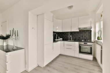 Beyaz dolaplar, siyah arka plan ve işlevsellik ve estetik için tasarlanmış çağdaş aletlerin yer aldığı şık ve şık bir mutfak..