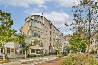 Yeşillik ve kaldırım ile çevrili, kentsel yaşam ve mimari sergilenen, mavi gökyüzüne karşı çağdaş bir yerleşim yapısı vurgulanır..