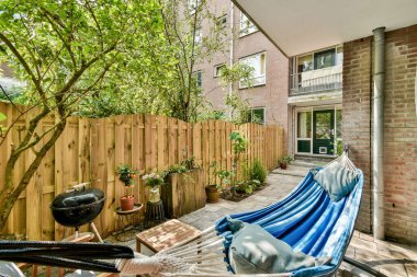 Mavi çizgili bir hamak, yemyeşil bir çit ve rahatlamak ve doğanın tadını çıkarmak için mükemmel bir ahşap çit içeren rahat bir açık hava alanı..