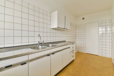Pürüzsüz ve minimalist bir mutfak. Temiz çizgiler, fayanslı duvarlar ve modern armatürler. Tasarım işlevselliği ve basitliği vurgular.