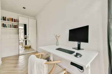 Minimalist bir masa, bilgisayar ve şık bir kitaplığın bulunduğu parlak, havadar, ahşap döşemeli bir oda..