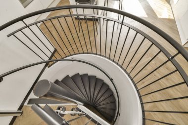 Pürüzsüz siyah korkulukların ve parlak ahşap zeminin yer aldığı modern spiral bir merdivenin büyüleyici görüntüsü. Tasarım, çağdaş mimari ve estetiği vurguluyor..