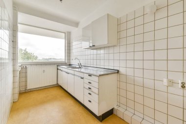 Beyaz fayanslardan oluşan parlak ve basit bir mutfak, işlevsel dolaplar, ve pencereden sakin bir manzara, minimalist tasarım prensiplerini somutlaştıran.
