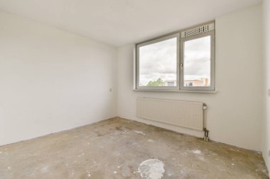 Geniş, dağınık bir oda beyaz duvarları ve geniş bir penceresi olan doğal ışığın içeri girmesine izin veren. Zemin çıplak, minimalist estetik sergileniyor..