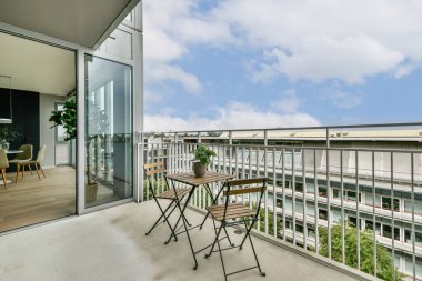 Şık oturma düzenleri, büyük cam pencereler ve kentsel yaşam deneyimini geliştiren saksı bitkilerinin yer aldığı çağdaş bir balkon..