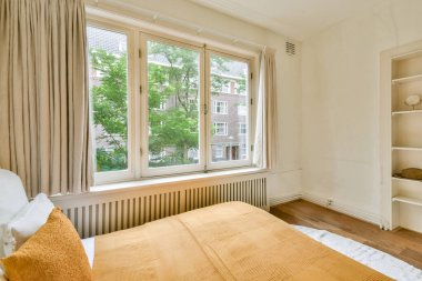 Sıcak dekore edilmiş bir iç mekan geniş pencereler, yumuşak tekstil ve doğal ışık modern ortamda sakin ve davetkar bir atmosfer yaratıyor..