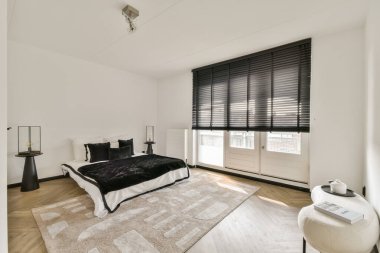 Zarif ve sakin bir yatak odası, minimalist dekorlar, siyah pencere örtüleri, ve sıcak ahşap döşemeler, şık bir atmosfer yaratıyor..