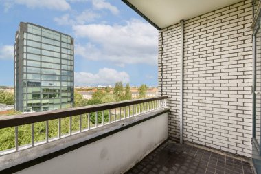 Şık, modern bir balkon çağdaş binalar ve verimli yeşilliklerle dolu canlı bir şehir manzarası, şehir yaşamını yüksek bir perspektiften gösteriyor..