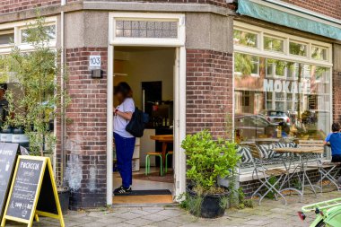Tuhaf bir kafe girişinde yeşil ve açık hava oturma yerleriyle çevrili ahşap bir kapı sergileniyor. Sıcak atmosfer, sıcak bir deneyim için müşterileri davet eder..