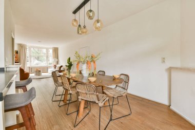 Doğal ahşap döşeme, zarif aydınlatma armatürleri ve çiçeklerle tamamlanmış şık rattan sandalyeler içeren parlak ve modern bir yemek alanı..