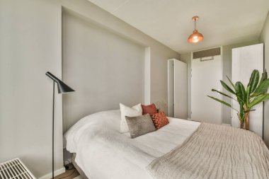 Dekoratif yastıklı, sıcak ışıklandırmalı ve minimalist dekoratif dekoratif bir ortam yaratan şık ve rahat bir yatak odası..