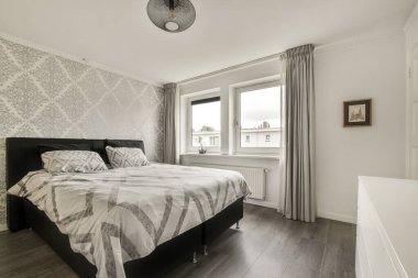 Parlak ve şık bir yatak odası. Duvar kağıtları, büyük pencereler ve modern mobilyalar. Huzurlu ve davetkar bir atmosfer yaratıyor..