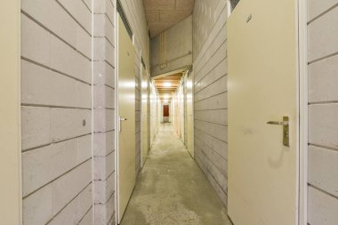 Ayrı odalara açılan kapılarla dolu geniş bir koridor, yukarıdaki ışıklarla aydınlatılıyor, derinlik ve perspektif hissi yaratıyor..