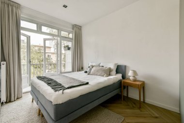 Rahat bir yatak odası, zarif bir komodin ve doğal ışığı davet eden büyük pencereler. Basit dekor sakinleştirici atmosferi artırır.