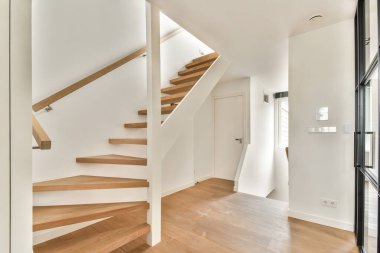 Ahşap merdiven ve temiz çizgilerle aydınlatılmış modern bir iç mekan geniş ve davetkar bir atmosfer yaratıyor..