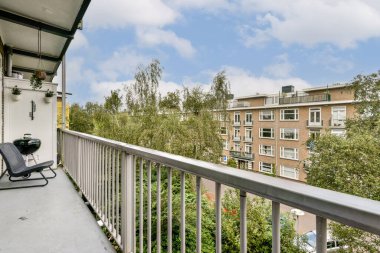 Berrak bir gökyüzünün altında yemyeşil ve kentsel mimarinin sergilendiği güzel bir balkon manzarası. Uzay, doğanın rahatlaması ve gözlemlenmesine davetiye çıkarır..