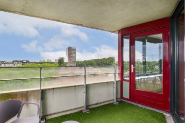 Yeşil çimenlerin olduğu modern bir balkon ve kısmen bulutlu bir gökyüzünün altındaki kentsel binaların çarpıcı manzarası. Açık hava ve şehir hayatının mükemmel bir karışımı..