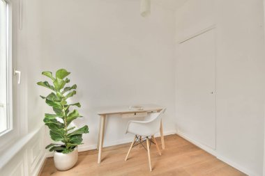 Sade ahşap bir masa, modern bir sandalye ve pencerenin yanında rahatlatıcı bir atmosfer yaratan yapraklı bir bitki içeren sakin ve parlak bir iç mekan..