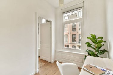 Beyaz duvarlar, ahşap döşemeler ve geniş pencerelerden akan bol miktarda doğal ışık içeren ve yeşil bir dokunuşla tamamlanan sakin bir minimalist iç mekan..