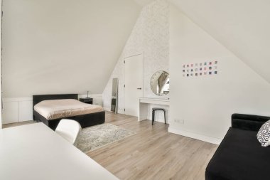 Pürüzsüz bir yatak, şık bir sandalye ve hafif ahşap döşeme ile tamamlanmış yuvarlak bir ayna içeren geniş, modern bir iç mekan. Tasarım minimalizmi vurguluyor..