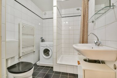 Beyaz bir çamaşır makinesi, zarif bir duş alanı ve minimalist tasarım elementleriyle tamamlanmış şık eşyalar içeren gösterişli modern bir banyo..