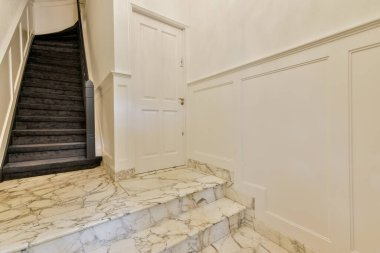 Güzel tasarlanmış mermer bir merdiven, modern mimari ve klasik zarafetin bir karışımını iyi aydınlatılmış bir koridorda sergileyen bir kapıya götürür..