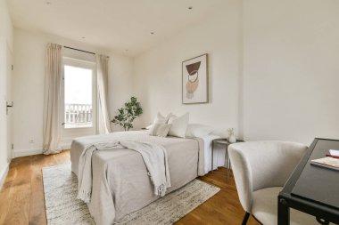 Minimalist tasarım elementleri, nötr renkler ve doğal ahşap aksanları olan iyi ışıklandırılmış modern bir yatak odası. Yer havadar ve davetkar..