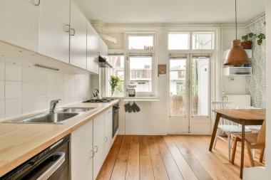Minimalist tasarım, ahşap döşeme ve geniş pencerelerden akan doğal ışık içeren parlak ve havadar bir modern mutfak davetkar bir atmosfer yaratıyor..