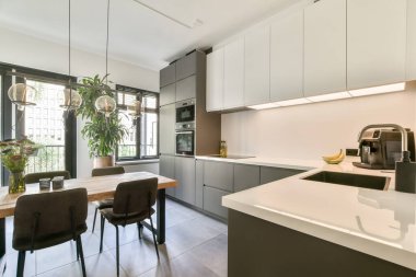 Minimalist dolapların ve şık mobilyaların yer aldığı, geniş pencerelerden gelen doğal ışıkla aydınlatılmış, gösterişli, modern bir mutfak. Hoş bir atmosfer yaratıyor..