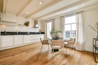 Ahşap döşemeleri, parlak doğal ışığı ve minimalist dekorları olan, günlük yemek ve toplantılar için mükemmel geniş bir iç mekanı olan gösterişli, modern bir mutfak..