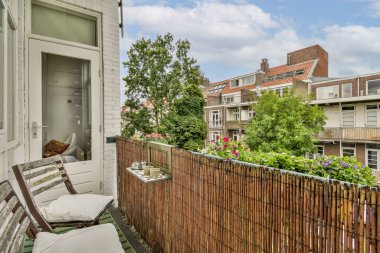 Bitkiler ve çiçeklerle süslenmiş rahat bir balkon kentsel bir ortamda huzurlu bir kaçış sağlıyor. Manzara doğa ve şehir mimarisinin bir karışımını sunuyor..