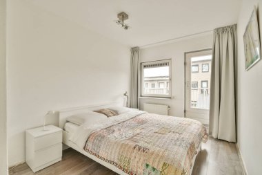 Çağdaş, şık bir yatak odası. Basit bir yatak odası, aydınlık duvarlar ve geniş bir pencereden gelen doğal ışık, sakin bir atmosfer yaratıyor..