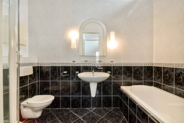 Zarif siyah fayansların, modern bir küvetin ve sofistike ışıklandırmanın olduğu şık bir banyo. Tasarım lüks ve temizliği vurguluyor..