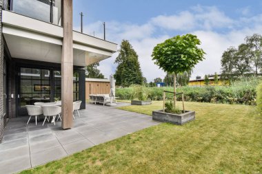 Güzel manzaralı bir bahçe, veranda alanı ve canlı bir yeşillik barındıran modern bir ev, sakin bir açık hava alanı yaratıyor..