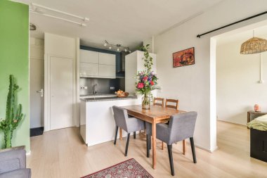 Modern bir mutfak ve yemek odası şık mobilyalar, bir kaktüs bitkisi ve canlı çiçekler, yemekler ve toplantılar için davetkar bir atmosfer yaratıyor..
