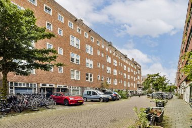 Açık gökyüzü altında park halindeki bisiklet, araç ve modern apartmanlarla dolu bir şehir caddesi manzarası, şehir yaşam tarzı ve mimarisini gözler önüne seriyor..