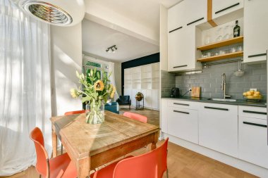 Modern bir mutfak, şık bir dolap, ahşap bir yemek masası ve canlı bir çiçek aranjmanı, sıcak ve davetkar bir atmosfer yaratıyor..