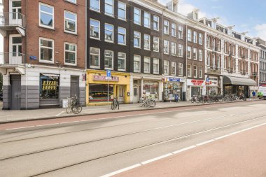 Geleneksel mimari, canlı dükkanlar ve açık mavi gökyüzünün altındaki yolları kaplayan bisikletlerin yer aldığı pitoresk bir Amsterdam caddesi..