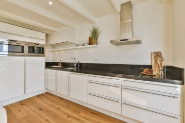 Beyaz dolaplar, paslanmaz çelik aletler ve sıcak ahşap döşeme içeren gösterişli ve modern mutfak. İşlevsellik ve tarzın mükemmel bir karışımı.