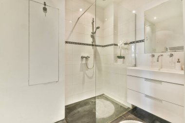 Cam duş muhafazası olan şık bir banyo, şık modern eşyalar ve zarif beyaz fayanslar, temiz ve çağdaş bir estetik yaratıyor..